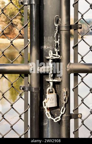 A closeup vertical shot of a lock on a chain link gate with the ocean in the background on a sunny day Stock Photo