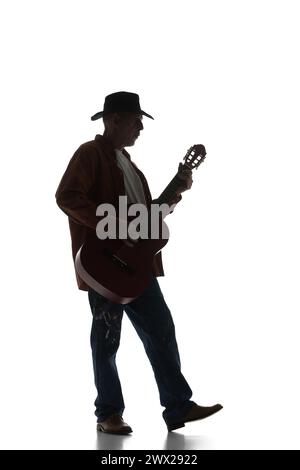 Silhouette of man in fedora hat playing guitar, performing isolated on white background. Black and white image. Stock Photo