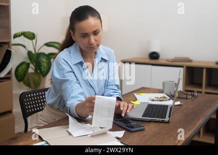 lady at home, holds a bill with laptop online payments. calculate taxes, review accounts, loan rate Stock Photo