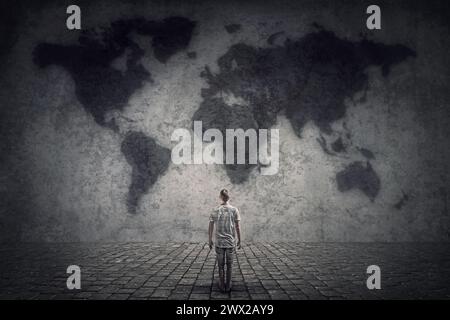 Person stands in front of a concrete wall looking at the world map. Travel limitations concept Stock Photo