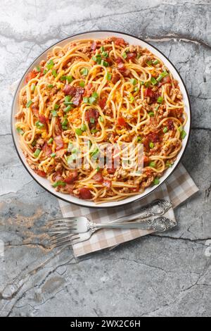 Western Cowboy Spaghetti with the addition of Ground beef, bacon, cheddar cheese, onion and hot sauce closeup on the plate on the table. Vertical top Stock Photo