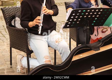A closeup plane of street orchestra flautist with flute in her hands. Street music band performing on old city background. Close up women playing flut Stock Photo