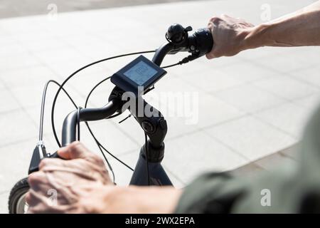 unrecognizable young man rides e-bike, hands holding bicycle handlebars Stock Photo