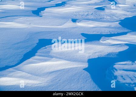 This serene winter scene showcases a vast expanse of snow-covered ground, with the sun casting deep shadows that highlight the intricate patterns form Stock Photo