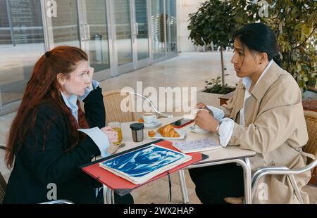 Two professionals engage in a serious business discussion over a morning coffee at an outdoor cafe setting. Stock Photo
