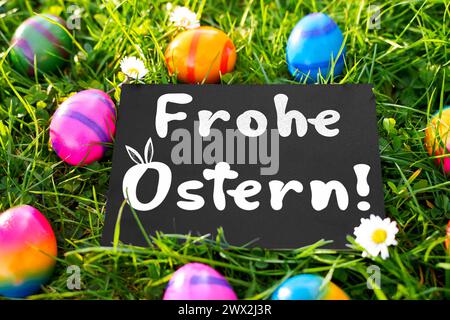 27 March 2024: Easter greetings: Happy Easter Lettering on a board in a green meadow with colorful Easter eggs. PHOTOMONTAGE *** Ostergrüße: Frohe Ostern Schriftzug auf einer Tafel in einer grünen Wiese mit bunten Ostereiern. FOTOMONTAGE Stock Photo