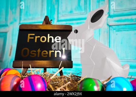 March 27, 2024: Easter greetings: Happy Easter Text on a plaque next to an Easter bunny in straw with Easter eggs. PHOTOMONTAGE *** Ostergruß: Frohe Ostern Text auf einer Tafel neben einem Osterhasen in Stroh mit Ostereiern. FOTOMONTAGE Stock Photo