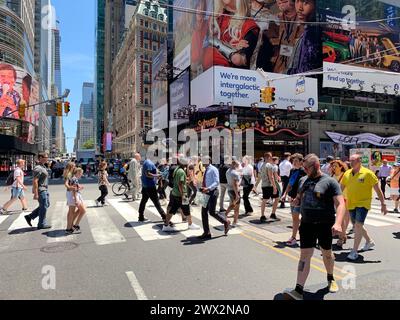 A crowd of people cross the street in the heart of New York City Times Square, surrounded by the billboards and advertisements Stock Photo