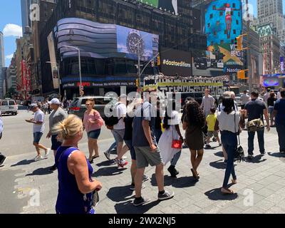 A large group of pedestrians cross the street at the crosswalk in the heart of New York City's Times Square Stock Photo