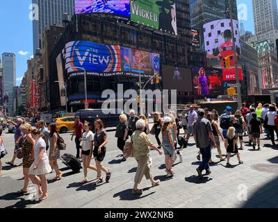 A large crowd of tourists and families walk across the street in New York's Times Square Stock Photo