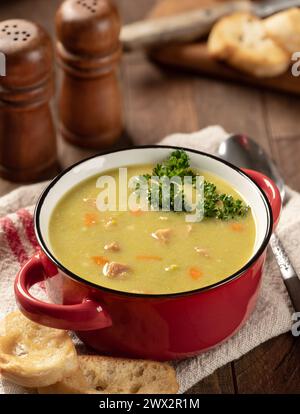 Bowl of split pea soup with ham and carrots garnished with parsley and toasted baguette on a wooden table Stock Photo