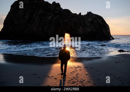 Sunset illuminates person in front of Window in the Rock feature of Keyhole Arch at Pfeiffer Beach in Big Sur on the Pacific Ocean in California, USA. Stock Photo
