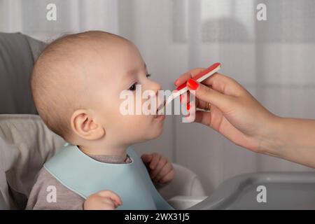 The first feeding with fruit puree for a baby boy who is 6 months old. Stock Photo