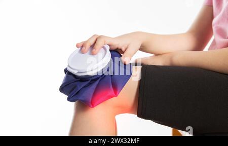 A girl applies a blue medical bag with ice to her knee joint for a knee injury. Local cryotherapy. Pain relief with cold. Stock Photo