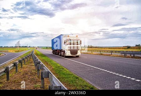 A container truck with a semi-trailer transports cargo from a port to another country along the highway in the summer. Stock Photo