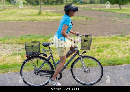 Happy mixed racial woman with virtual reality goggles cycling in nature. Stock Photo