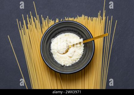 A black bowl with grated cheese on a pile of dry spaghetti pasta Stock Photo