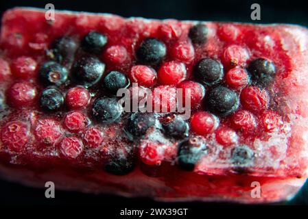 Mixed red and black berries frozen in an ice block against a black background. Stock Photo