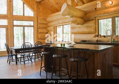 Island with dark grey granite countertop and black stained wooden bar stools plus antique wood table with rounded high back chairs in in open concept Stock Photo
