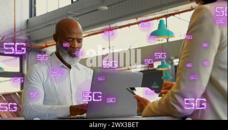 Image of multiple 5g texts over diverse coworkers working on laptop and digital tablet. Digital composite, multiple exposure, business, telecommunicat Stock Photo