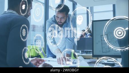 Image of icon in circles over diverse architects discussing about floor plan on blueprint. Digital composite, multiple exposure, report, business, glo Stock Photo