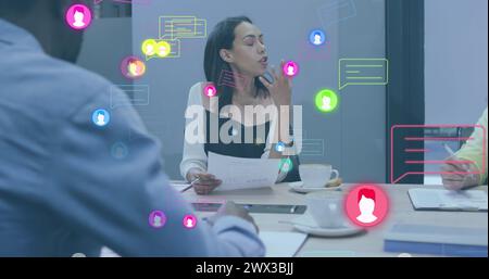 Image of profile icons and message boxes over diverse woman sharing ideas with coworkers. Digital composite, multiple exposure, business, planning, di Stock Photo