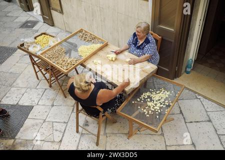 two women making traditional fresh pasta called 'orecchiette' in a street of Bari Old Town Stock Photo