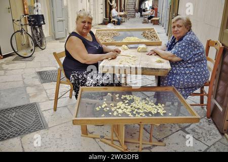 OLD BARI, ITALY - JULY 06: mother and daughter making traditional fresh pasta in the street 'Arco Basso' of Bari Old Town, also known as the street of Stock Photo