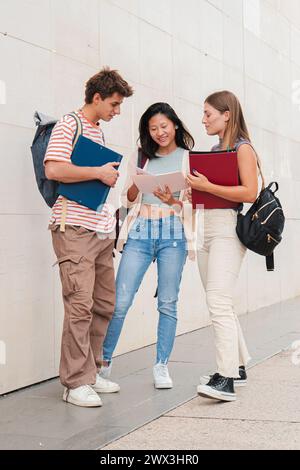 Vertical. Group of classmates talking about the class, standing at university campus. Three real students having a friendly conversation about the high school homework. Young academy people speaking. High quality photo Stock Photo