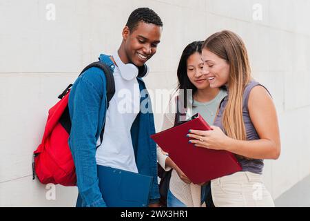 Group of classmates talking about the class, standing at university campus. Three real students having a friendly conversation about the high school homework. Young academy people speaking together. High quality photo Stock Photo
