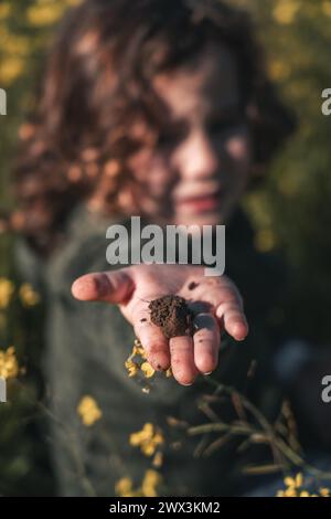 detail portrait of piece of earth in the hand of a little boy who shows it to the camera happy and content on bright sunny day on green meadow Stock Photo