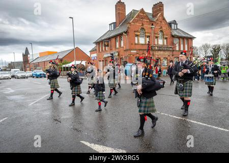 vehicles are halted as Warrington Pipe Band crosses through traffic lights during the 2024 St Patrick's Day parade Stock Photo