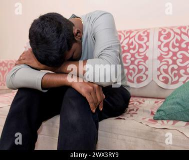 A thoughtful Indian man sits alone on a couch in his living room, deep in thought or contemplation. Stock Photo