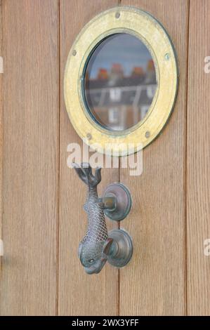Traditional dolphin shaped brass door knocker under a porthole shaped window in a wooden door on this harbourside house in Weymouth, Dorset. Stock Photo