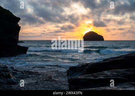 The sun setting behind Gull Rock Island. Trebarwith Strand Beach with Gull Rock Island, dramatic cliffs, rocks and sea at sunset. Stock Photo