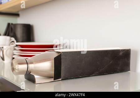One metal thermos bottle with paper box and dishes on shelf, macro. Stock Photo