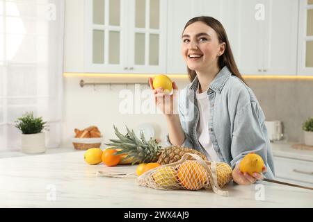 Woman with lemons and string bag of fresh fruits at light marble table in kitchen Stock Photo