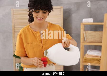Happy woman pouring laundry detergent into cap indoors Stock Photo