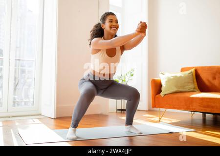 lady athlete performs squats and stretches her arms forward indoor Stock Photo
