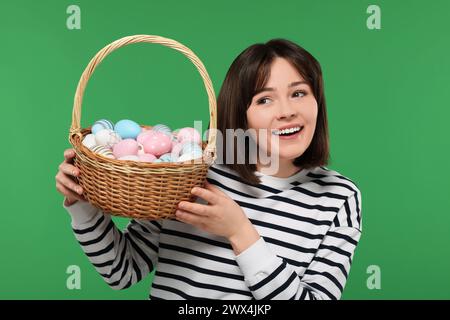 Easter celebration. Happy woman with wicker basket full of painted eggs on green background Stock Photo