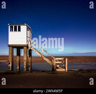 A view at night under moonlight with a clear sky and the northern lights of the refuge hut on the causeway on Lindisfarne in Northumberland Stock Photo