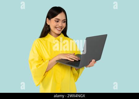 Young happy hispanic lady using laptop, typing report marketer, isolated at blue color background.  Stock Photo