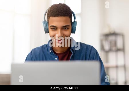 Happy teen guy with headphones using laptop and smiling Stock Photo