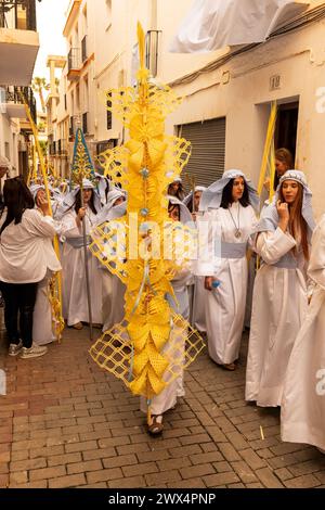 Almuneca, Spain.  Easter week in Almuneca, Spain commences with the first major event is Palm Sunday (Domingo de Ramos), the holiday held exactly one week before Easter Sunday, commemorating Jesus' famed entry into Jerusalem on a donkey. The brotherhoods organise the processions that parade through the streets and squares every day carrying beautiful 'pasos' and 'tronos' adorned with flowers and religious images that are carried on the shoulders of the participants. In this image participants parade through the narrow streets and avenue's of Almuñécar  24th March 2024 David Smith/Alamy Stock Photo