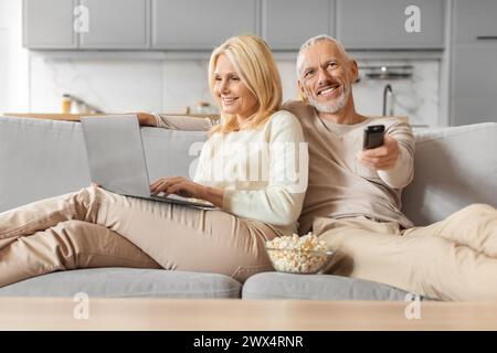 Mature couple using laptop and watching TV Stock Photo