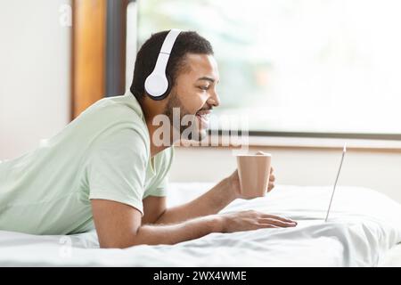 Man in bed with headphones using laptop Stock Photo