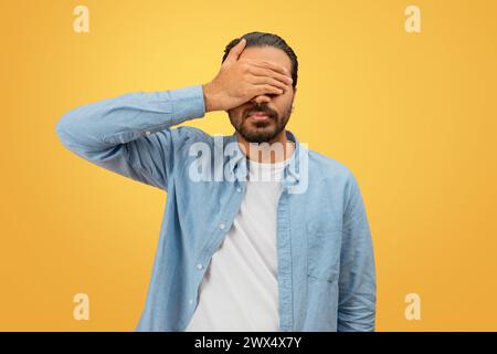 Man covering face with hand on yellow background Stock Photo