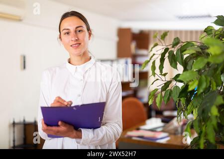 Portrait of a young female manager standing in a office and making notes Stock Photo