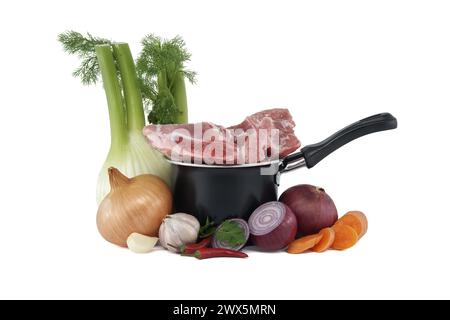 Black saucepan with pieces of raw pork atop. Around the saucepan are sliced vegetables which include onions, carrots, and garlic isolated on white bac Stock Photo