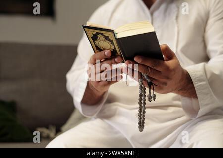 Medium closeup of hands of unrecognizable Muslim man holding misbaha reading Quran book Stock Photo